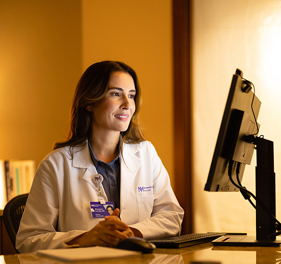 Female Northwestern Medicine physician wearing a lab coat and working on a computer.