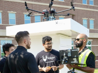 people conversing in a circle with a drone operator holding a laptop